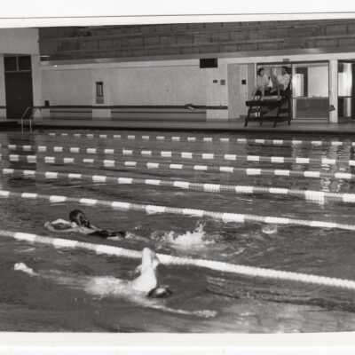 Students swimming in pool at sports recreation complex.