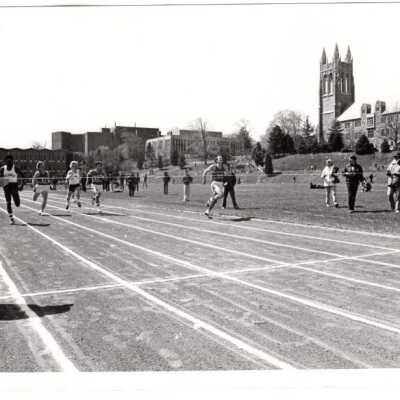 Men's track meet with Science Center, Drexel Library, and Barbelin in background and Coach Kevin Quinn and Emory Ross, S.J. on sideline.