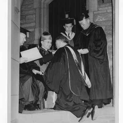 John J. O' Connor, S.J. kisses ring of Bishop Carroll McCormick during 1947 graduation/commencement ceremony. Others in photograph include: John J. Long, S.J., Dr. Distler, and Michael P. Boland?