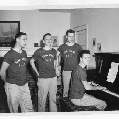 Four students from Barry Hall singing around piano.