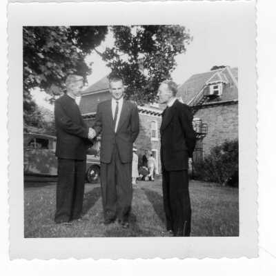 The first Proctors of Quirk Hall, Joseph J. Molloy, S.J. and Francis J. Emory, S.J. greeting James Kase of the Class of 1954, who was the first President of Quirk Hall, and who had become a Medical Doctor. Quirk Hall is in background. Photo collected by