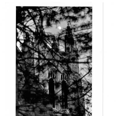 Exterior view of Barbelin Tower through evergreen tree limbs with moon in sky.