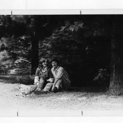 Two students sitting on lawn under pine trees.