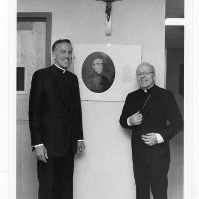 Donald I. MacLean, S.J. standing next to photo of Edward J. Sourin, S.J. at dedication of Sourin Residence Center.
