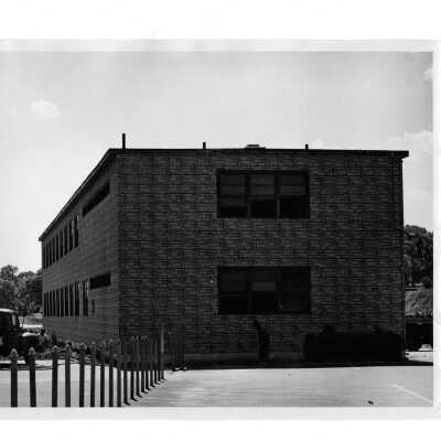 Exterior view of veterans barracks with workmen and pickup truck. Barracks located near Cardboard College also known as Barbelin Annex.