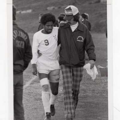 Injured men's soccer player being helped off the field.