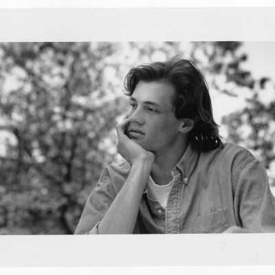 Male student sitting outside with trees in background.