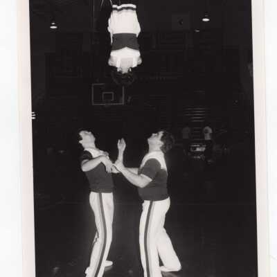 Two men cheerleaders flipping a woman cheerleader.