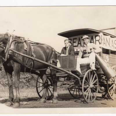 Two students, J. Lincoln Reinhardt and Gus Carr (?) driving covered wagon drawn by horse to advertise football game against Arkansas as student booster club/pep rally activity (?)