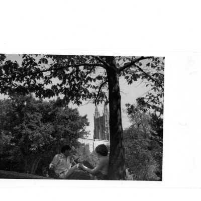 Two students sitting under tree with part of Drexel Library and Barbelin Tower in background.
