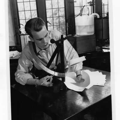 Charles Costello weighing sample sheets of paper on the Ellendorf balance in paper making (papermaking) school.