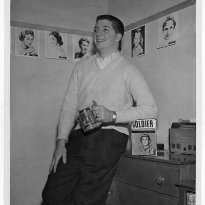 Student resident of Quirk Hall in dormitory room with photos of female movie stars on walls and book of memoirs on General Matthew Ridgway.