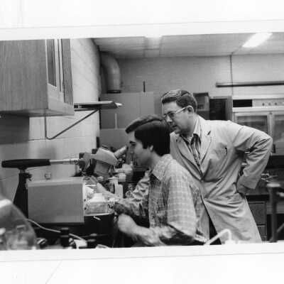 Student looking through microscope with instructor in science laboratory.