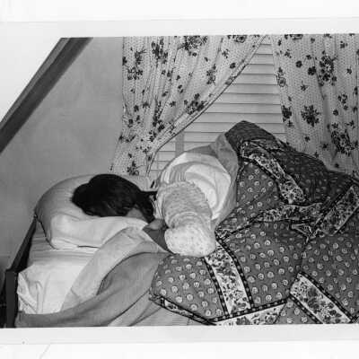 Woman student sleeping under comforter in dormitory room.