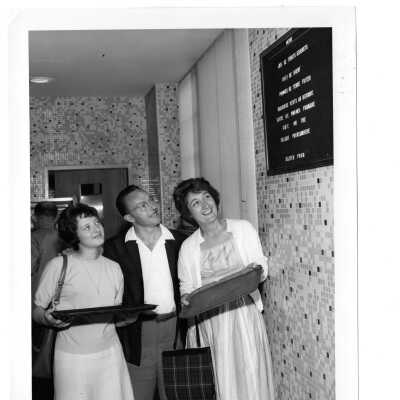 Man and two women holding trays looking at menu on wall of Campion cafeteria.