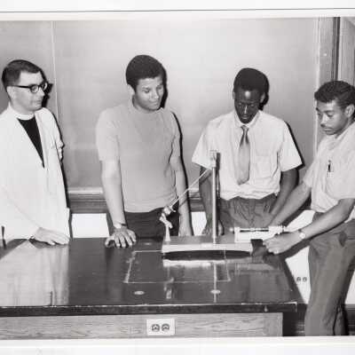 Physics professor, Howard Heim, S.J., working in laboratory with three high school students, 1970.