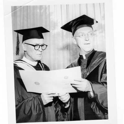 J. Joseph Bluett, S.J., looking at commencement program with guest during 1959 graduation/commencement.