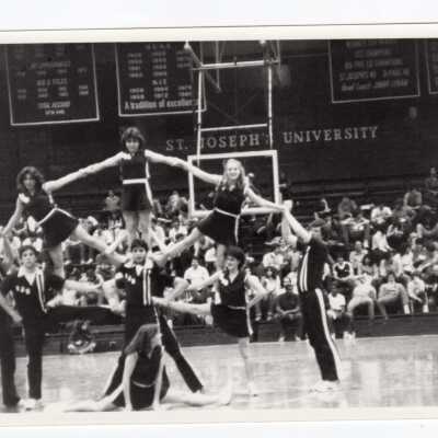 Men and women cheerleaders in pyramid during basketball game.