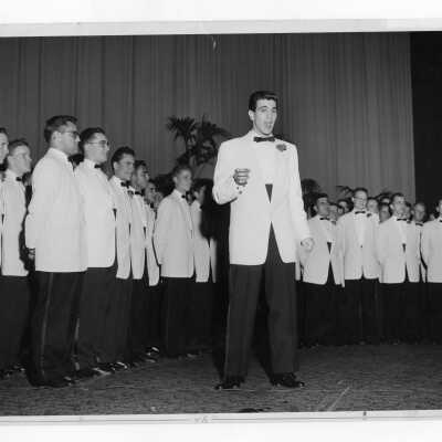 Members of Glee Club wearing white tuxedos giving concert in Flanigan Auditorium.
