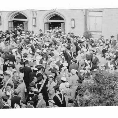 Crowd of graduates and guests outside Field House after 1956 graduation/commencement ceremony.