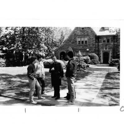 Terrence Toland, S.J., talking with three students in front of Regis Hall.