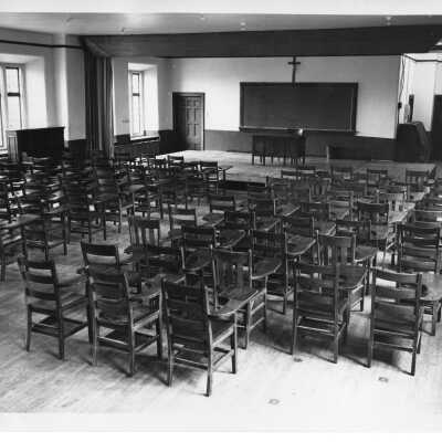 Interior view of classroom in Barbelin building with empty desks and podium with blackboard.