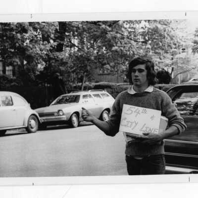 Student hitchhiking holding sign saying 54th and City Line.