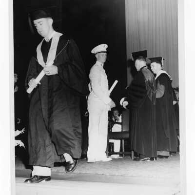 Edward G. Jacklin, S.J. and Michael Boland handing out diploma to two students including one dressed in military uniform, possibly Gordon Shockley, during 1955 graduation/commencement.