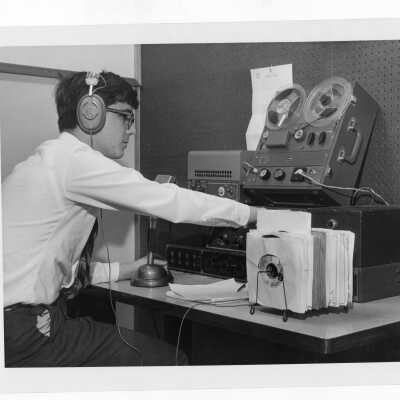 Student in Radio Club (Station WSJR?) sitting at table with microphone tape recorder, tape player, and forty-five rpm records.