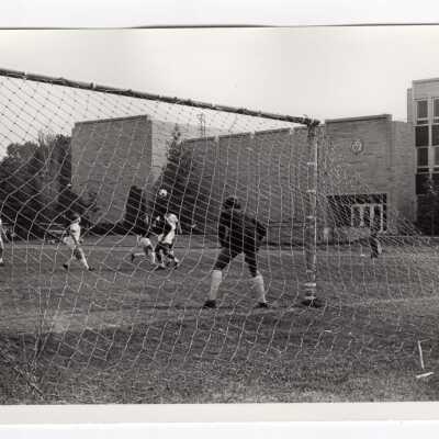 Men's soccer match with Post Hall in background.