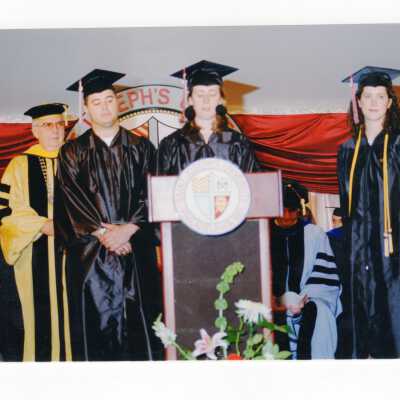 Graduating students addressing audience during 1999 graduation/commencement with Nicholas S. Rashford, S.J. in background.