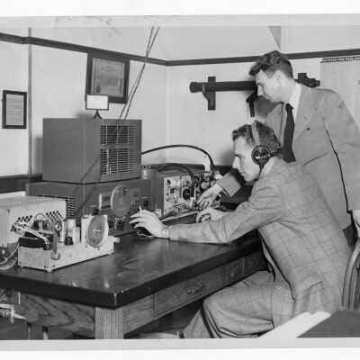 Two students in Radio Club working with equipment, one holding cigarette in hand. (Connected to Physics Department?)