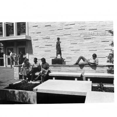 Exterior view of Villiger (later Post) Academy of Food Marketing with statue of Saint Joseph the Worker and students sitting on benches and wall talking.