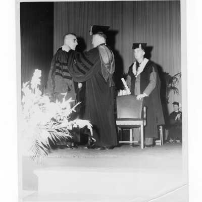 Edward G. Jacklin, S.J. conferring honorary degree on Joseph C. Cox, Sr. with Michael Boland standing nearby during 1955 graduation/commencement.