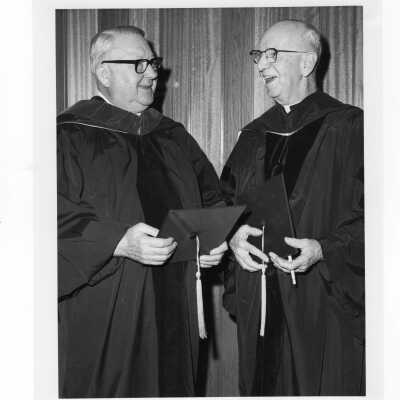 Dennis Comey, S.J., with honorary degree recipient, Harry Boyer (?) during convocation, December 17, 1975.