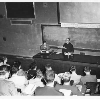 Interior view of physics amphitheater in Barbelin Longeran building with Jesuit faculty member and students listening to lecture.