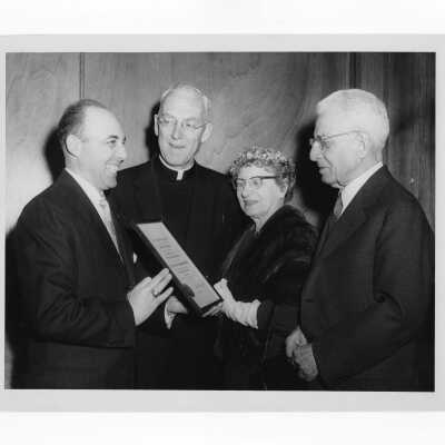 Dr. J. Parsons Schaeffer showing Shaffrey award certificate to J. Joseph Bluett, S.J., Mrs. J. Parsons Schaeffer, and others, 1959.