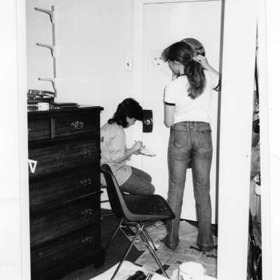 Two women students painting door in dormitory room.