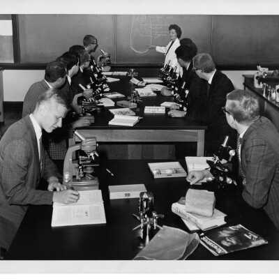 Biology professor, Catherine Nash, teaching class in science laboratory with students sitting at tables with microscopes, September 1963.