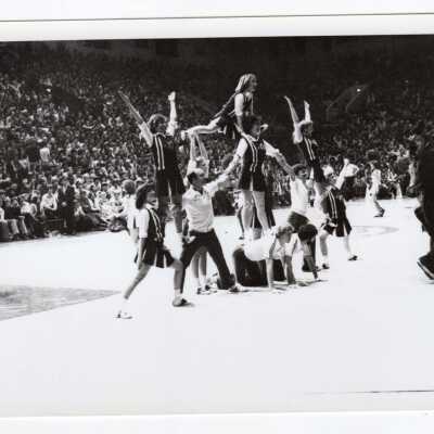 Men and women cheerleaders in pyramid at basketball game.