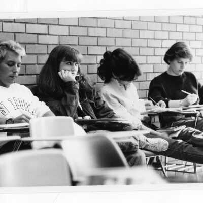 Several students sitting at desks in classroom listening to lecture.