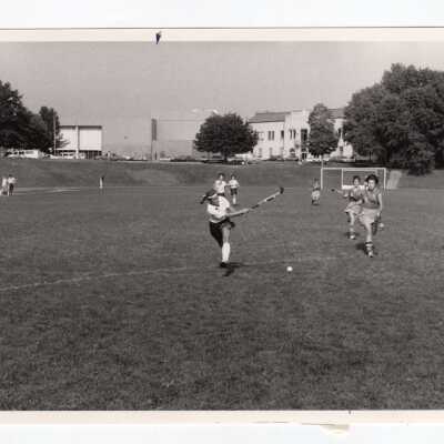 Women's field hockey match on Finnesey Field with Field House/Sports Complex in background.