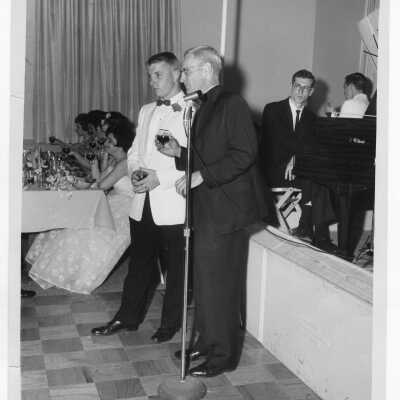 Student formal dance with Michael J. Smith, S.J., and student standing near microphone holding wine glasses.