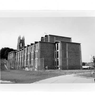 Exterior side view of Bellarmine with workmen in front and Barbelin Tower in background.