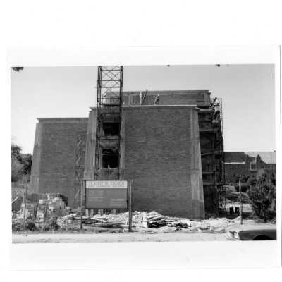 Exterior side view of Bellarmine under construction with two workmen on roof.