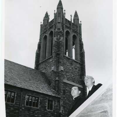 J. Joseph Bluett, S.J., (President) standing with another individual on steps with Barbelin tower in background.