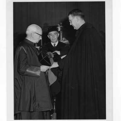 William F. Maloney, S.J., and Michael Boland help Monsignor Francis Brennan don his hood during convocation, September 13, 1962.