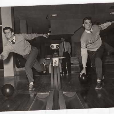 Two students bowling wearing sweaters, shirts, and ties as part of intramurals?