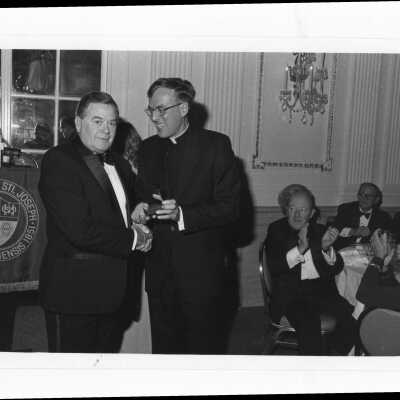 Donald I. MacLean, S.J., presenting award to Thomas J. Dugan at alumni awards dinner, c. 1980.