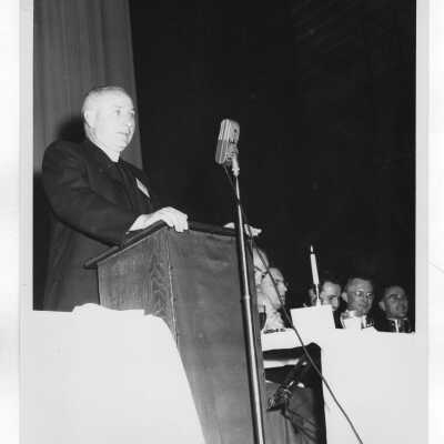 Joseph M. Geib, S.J.: Dean of Men, Director of Athletics. Fr. Geib is at podium addressing a banquet. Other faces that can be identified are: Edward Jacklin, S.J.; Joseph Pascucci; Matthew Quinn, S.J.
